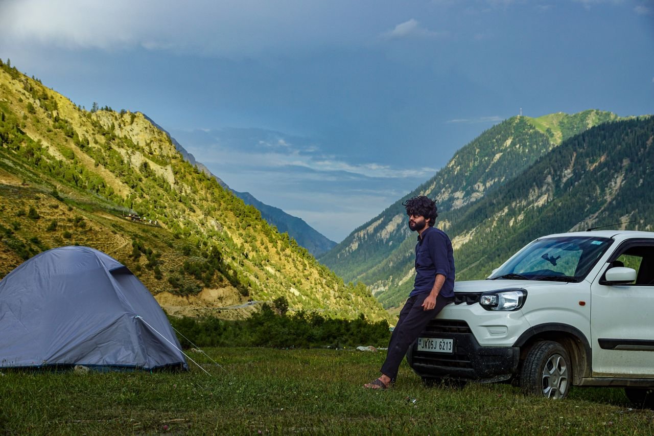 Man camping in Gurez Valley with a tent and car, surrounded by mountains and nature.
