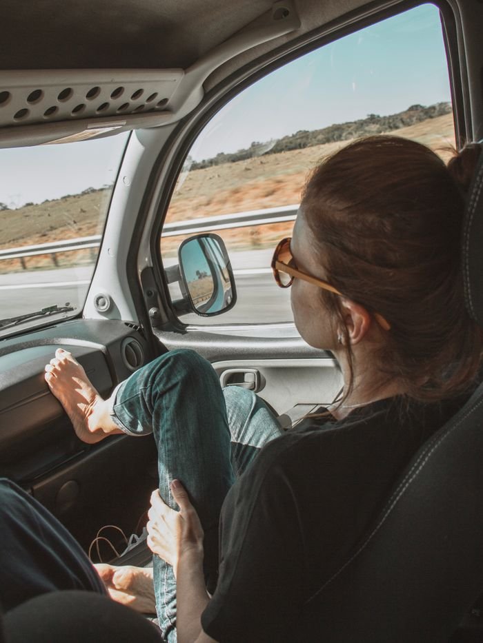 Woman relaxing in a car during a sunny road trip through São Paulo's scenic landscapes.