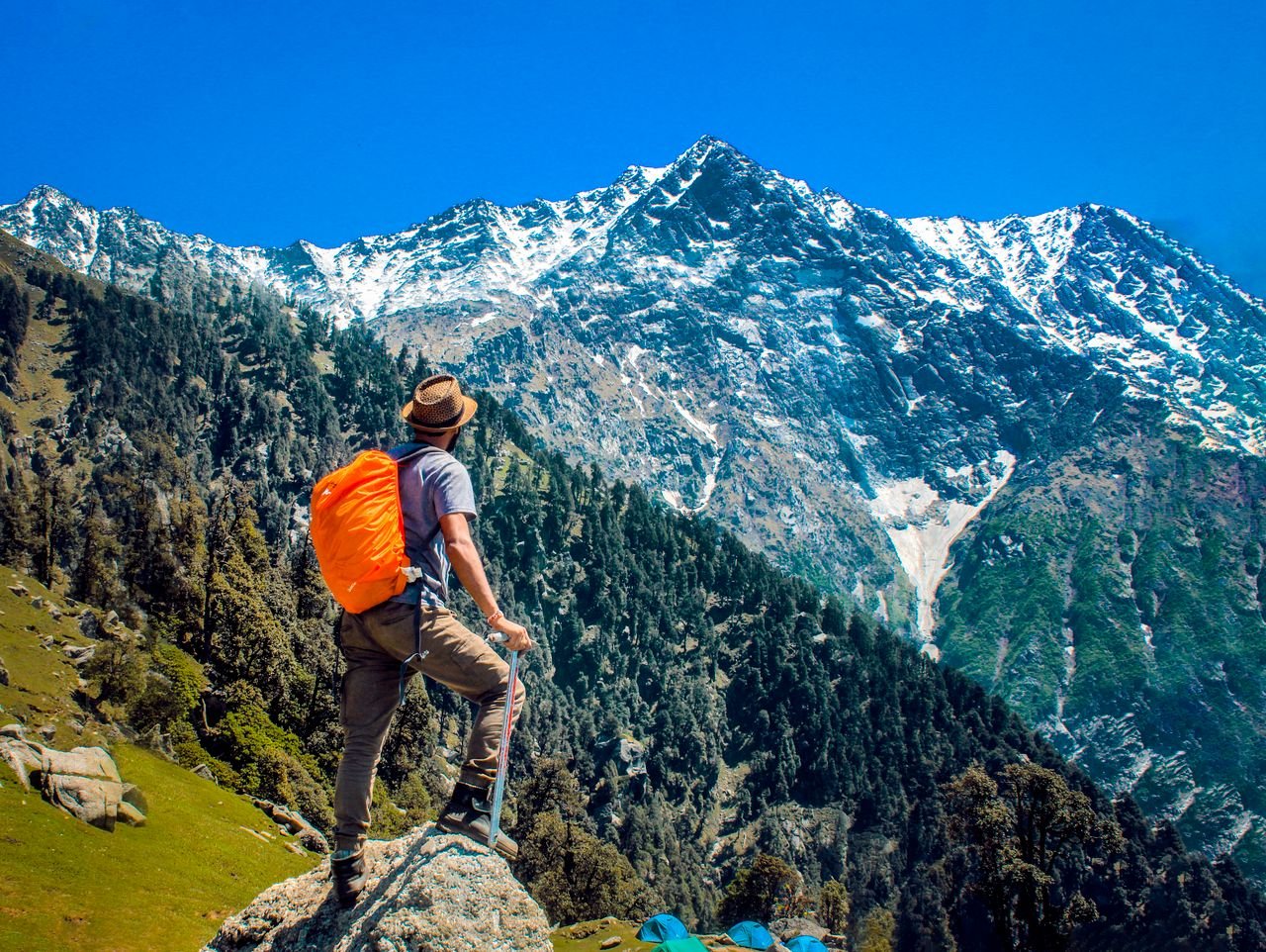 about-03 Man exploring breathtaking mountain scenery with snow-capped peaks under a clear blue sky.