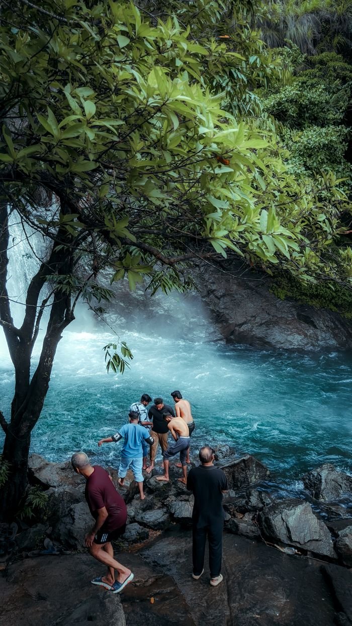 A group of people enjoying a picturesque waterfall, surrounded by lush greenery and rocky terrain.