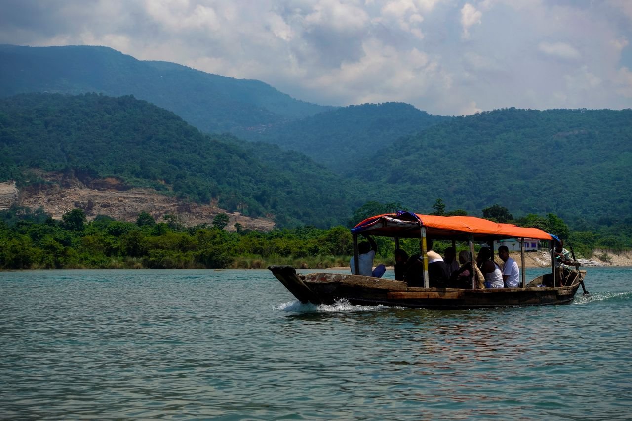 A traditional boat glides through picturesque waters in Sylhet, Bangladesh, amidst lush green mountains.
